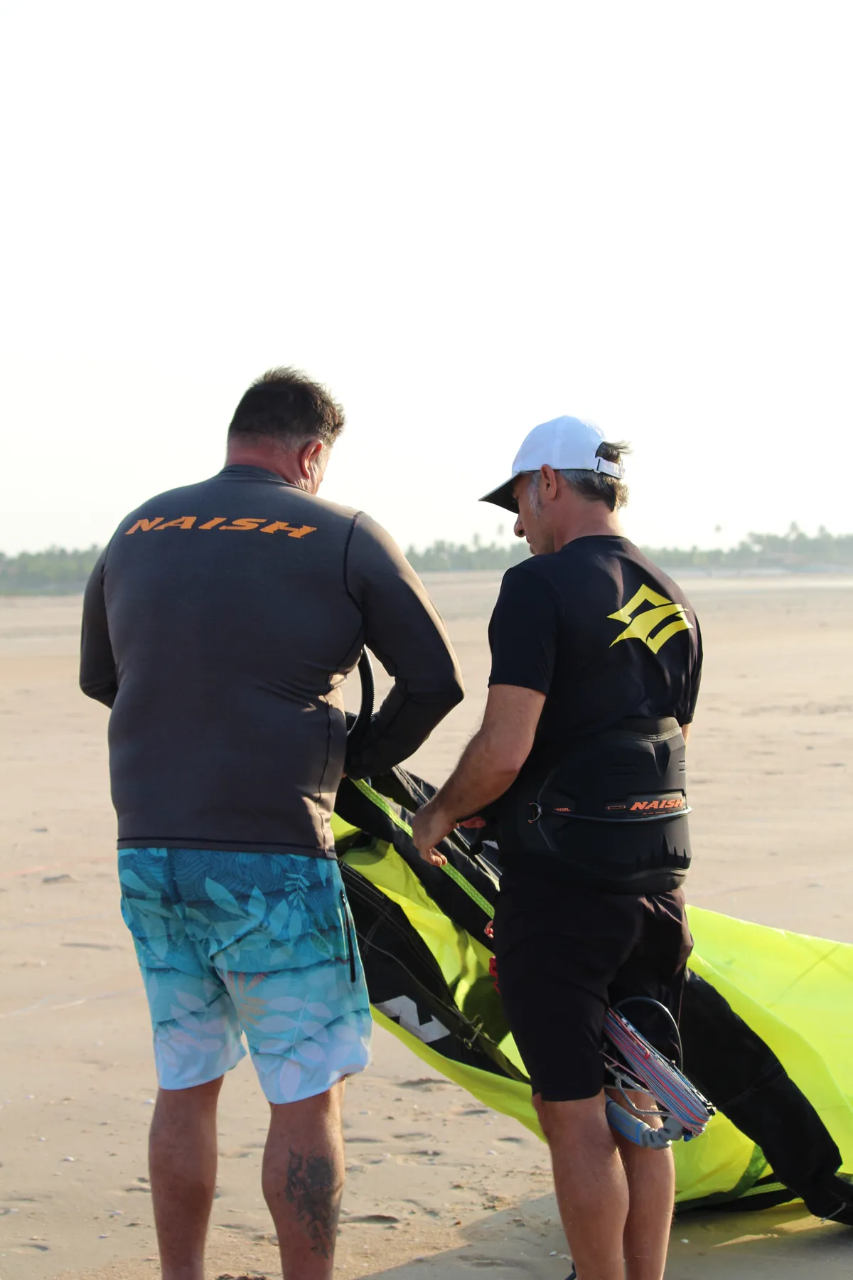 Dois instrutores com kites azul e verde conversando na praia da Ilha do Guajirú