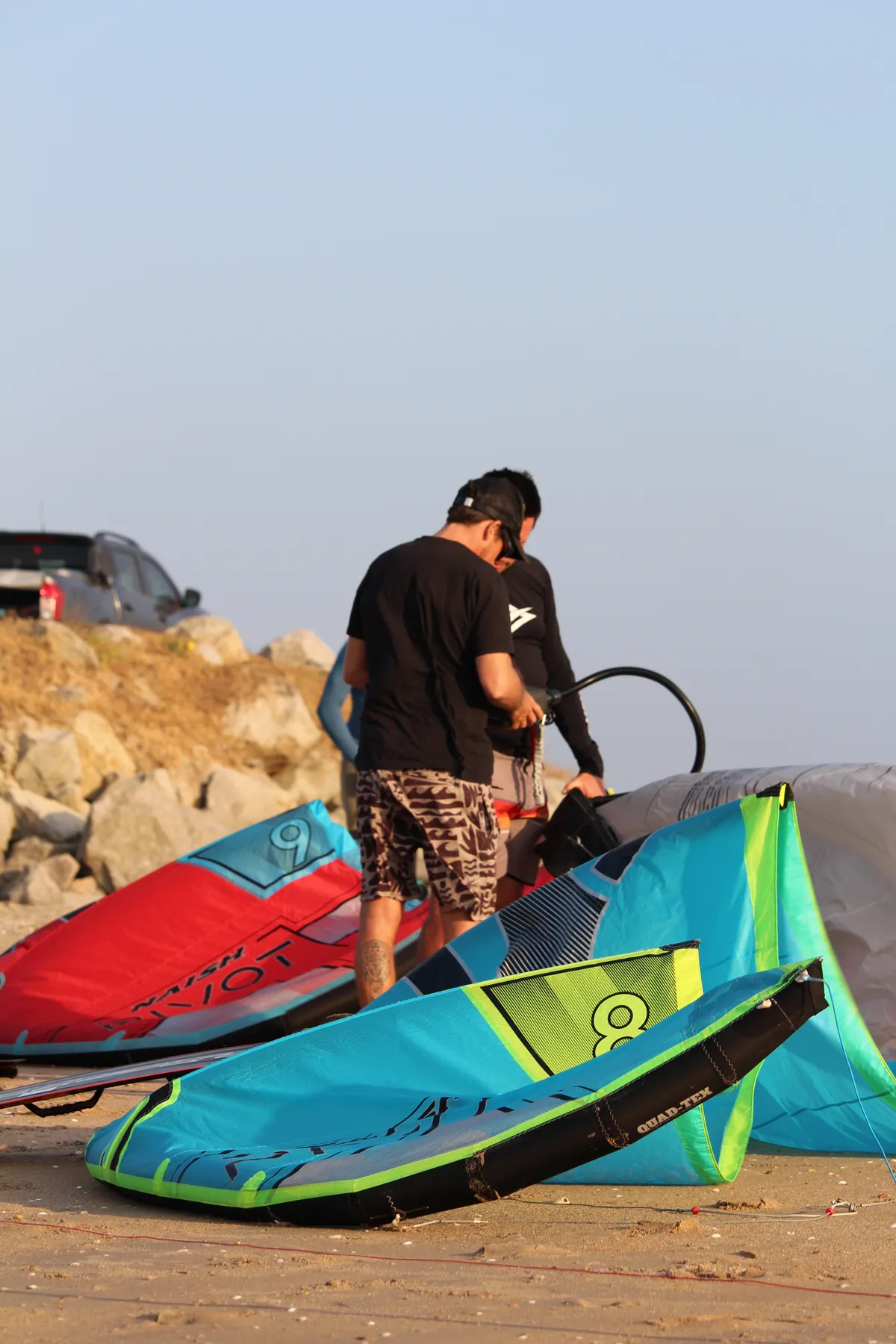 Instrutor auxiliando aluno na montagem de prancha Naish na praia da Ilha do Guajirú