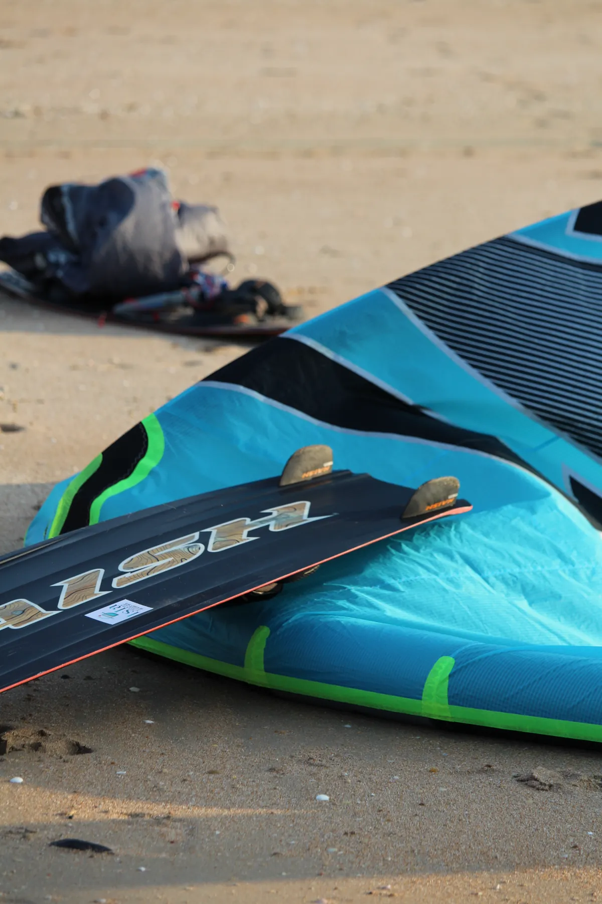 Prancha Naish azul e branca apoiada na areia da Ilha do Guajirú com o oceano ao fundo
