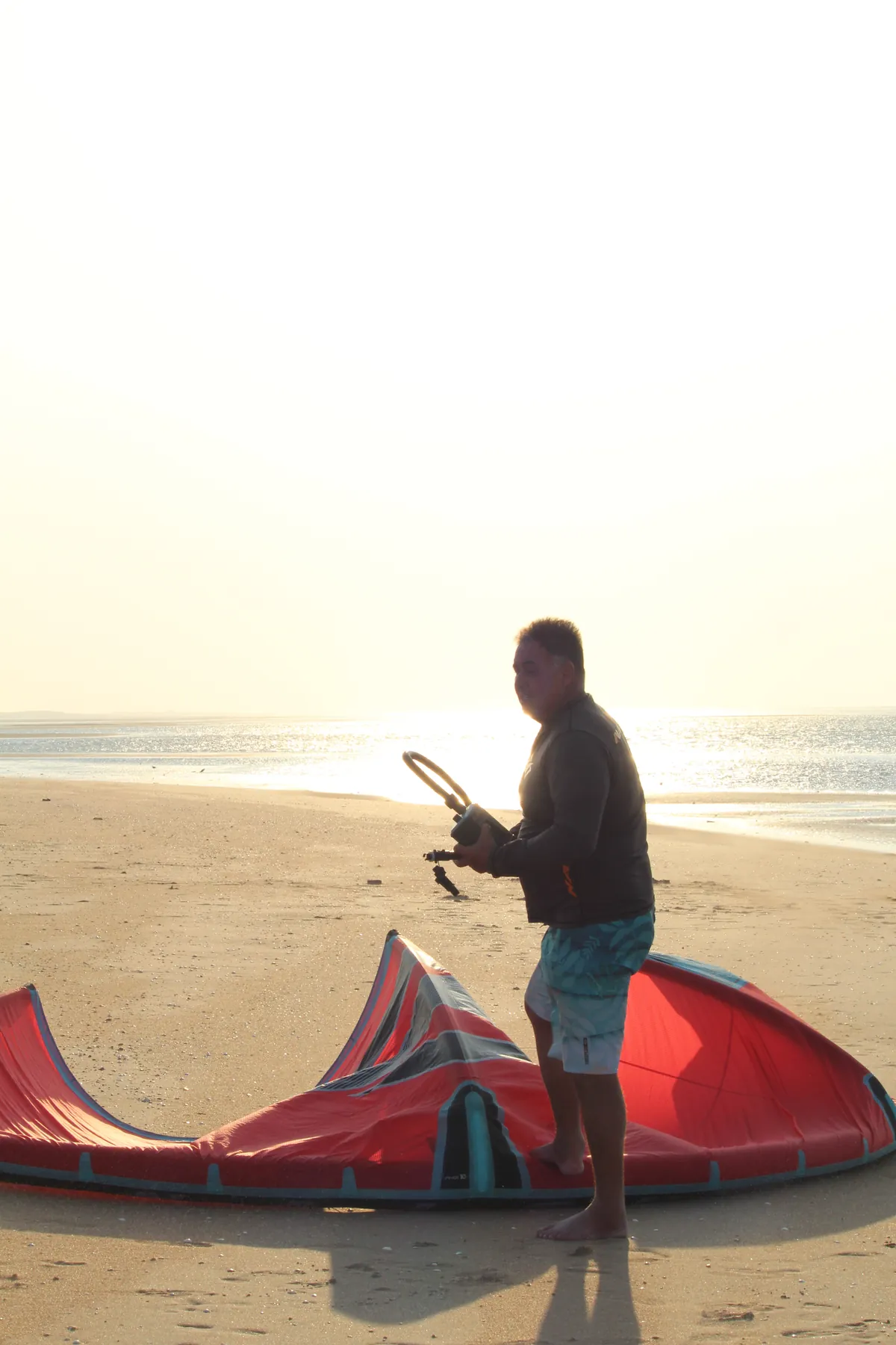 Instrutor preparando um kite vermelho na praia da Ilha do Guajirú ao entardecer