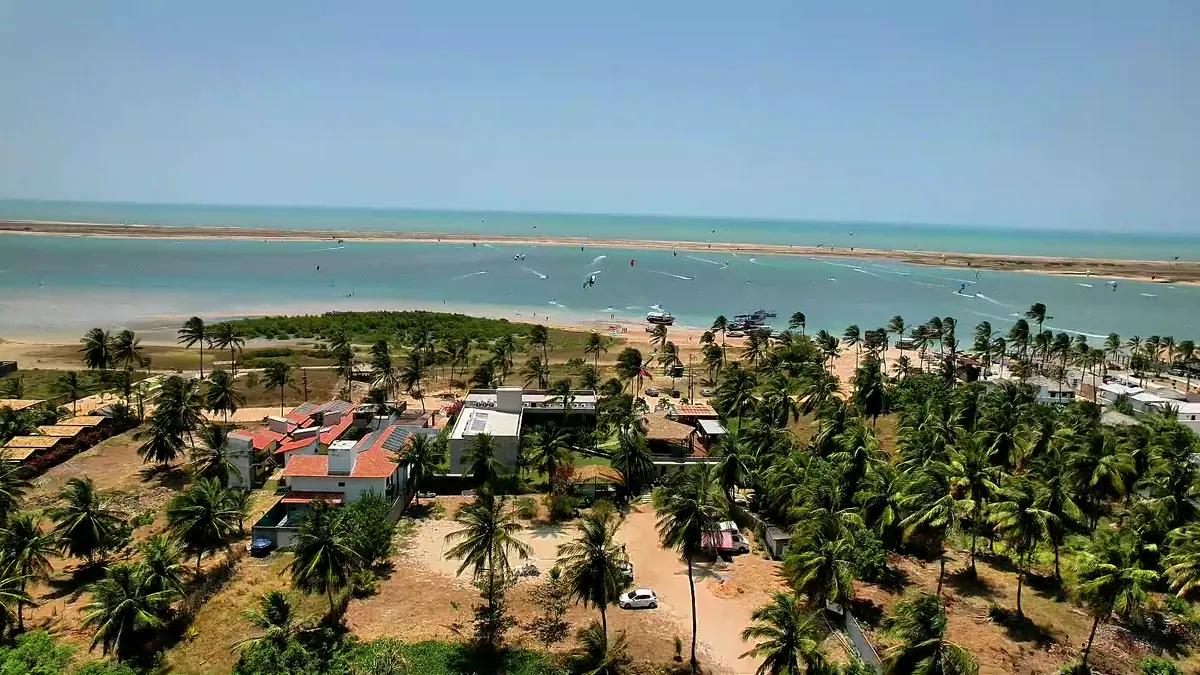 Vista aérea da Ilha do Guajirú em Itarema, no Ceará: o braço de mar, a vila entre coqueiros e kitesurfistas velejando na água plana