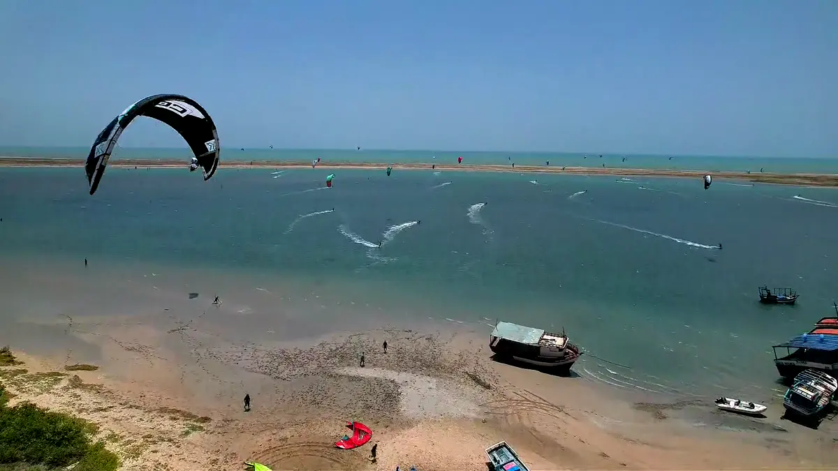 Kitesurfista cortando a água do braço de mar com spray, coqueiros da Ilha do Guajirú ao fundo